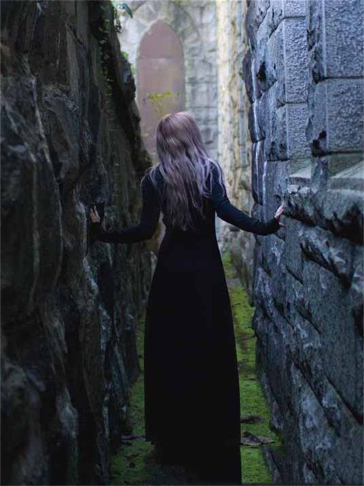 A woman wearing Gothic Long Sleeve Dress - Vintage Black Train Skirt Style Standing between two walls, with her back to the camera